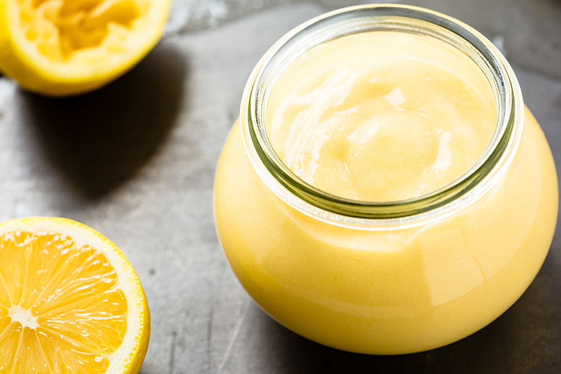 Homemade lemon curd in glass jar on fresh lemon background